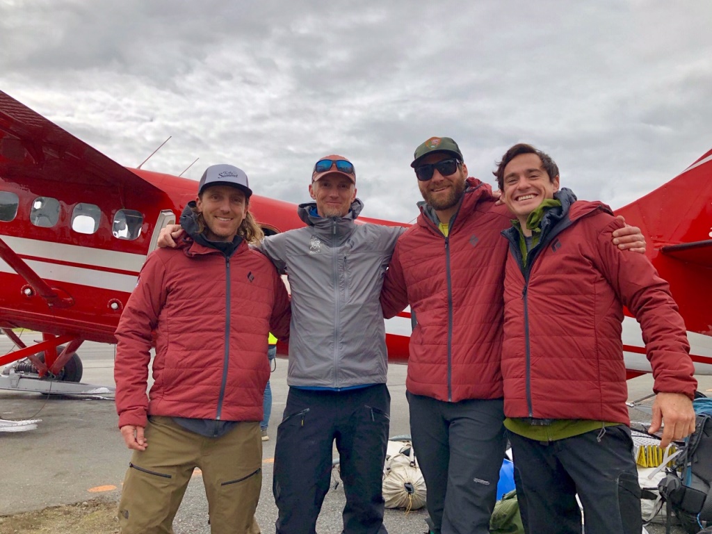 Four mountaineers pose for a photo outside an awaiting airplane