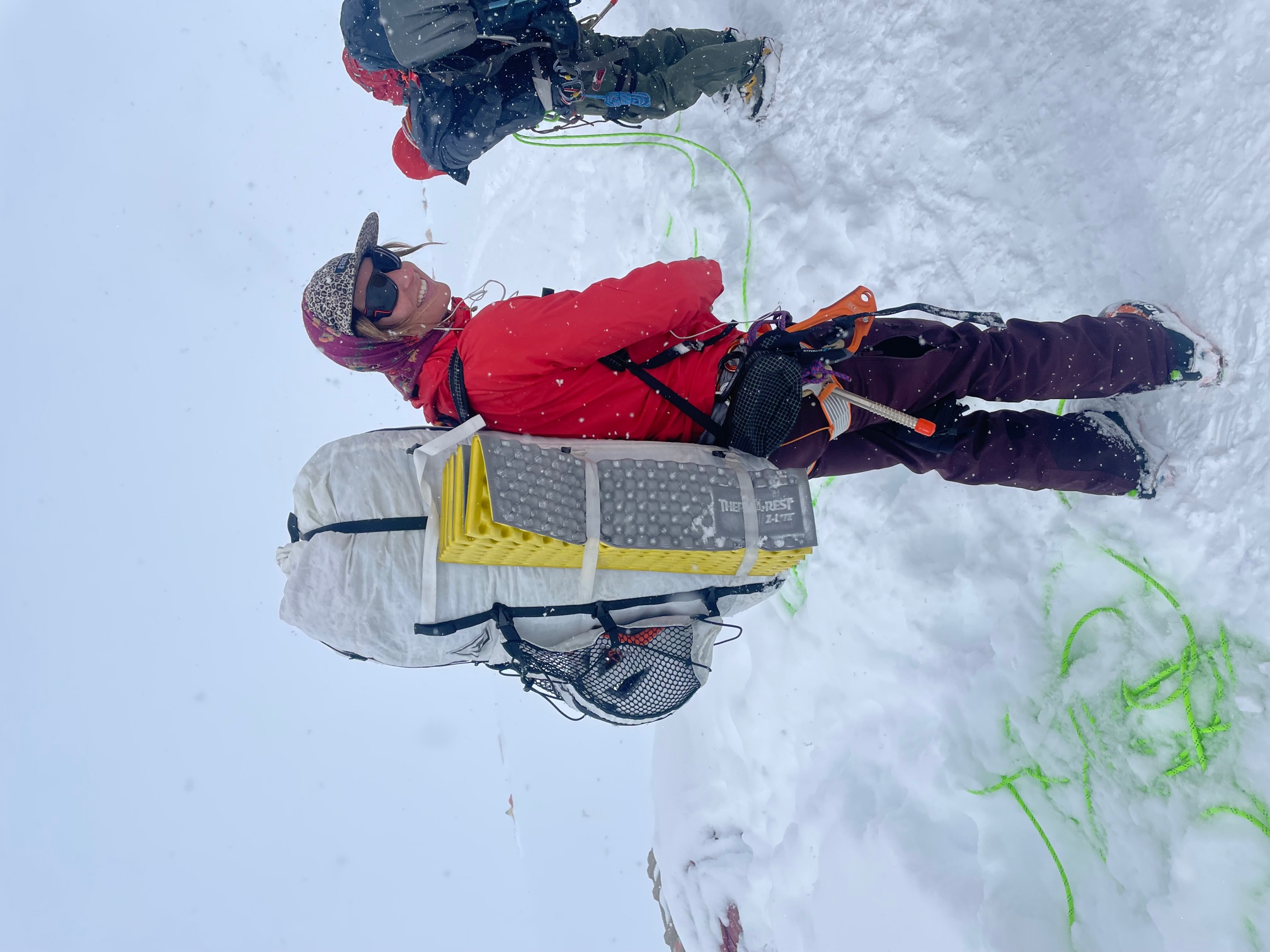 A slender woman stands in camp with an enormous backpack.