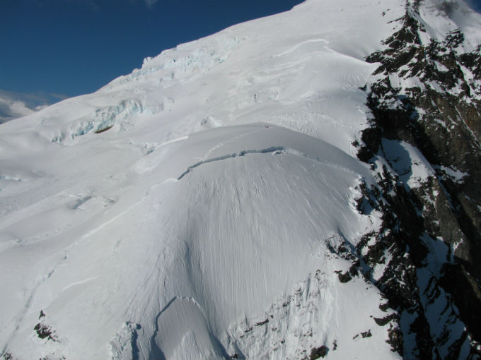 Climbers standing in snow field above avalanche debris