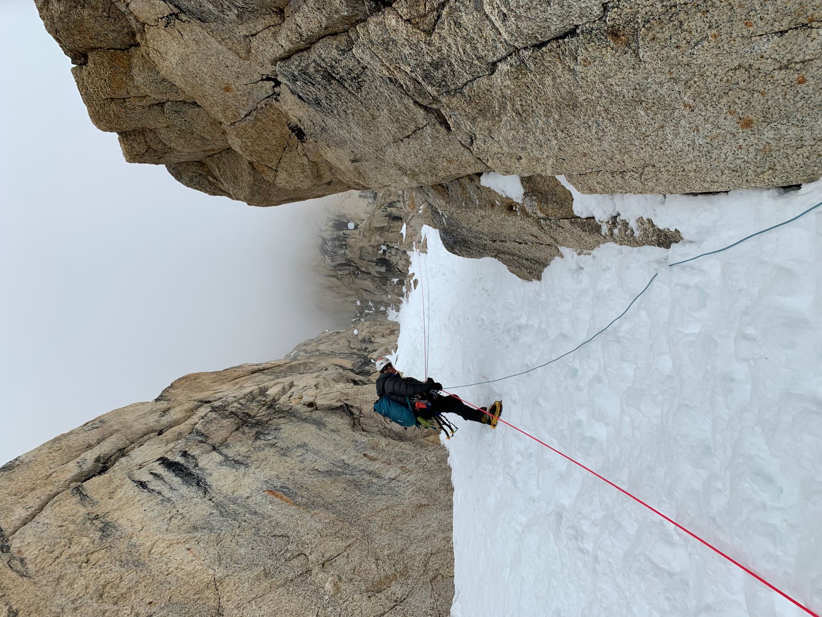 A roped climber peers down from a snow gulley lined with steep rock walls