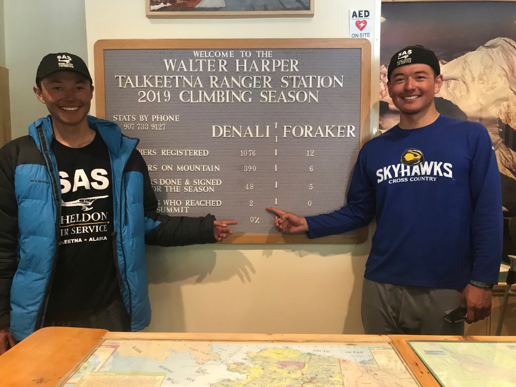 Two smiling climbers stand in front of a statistics board