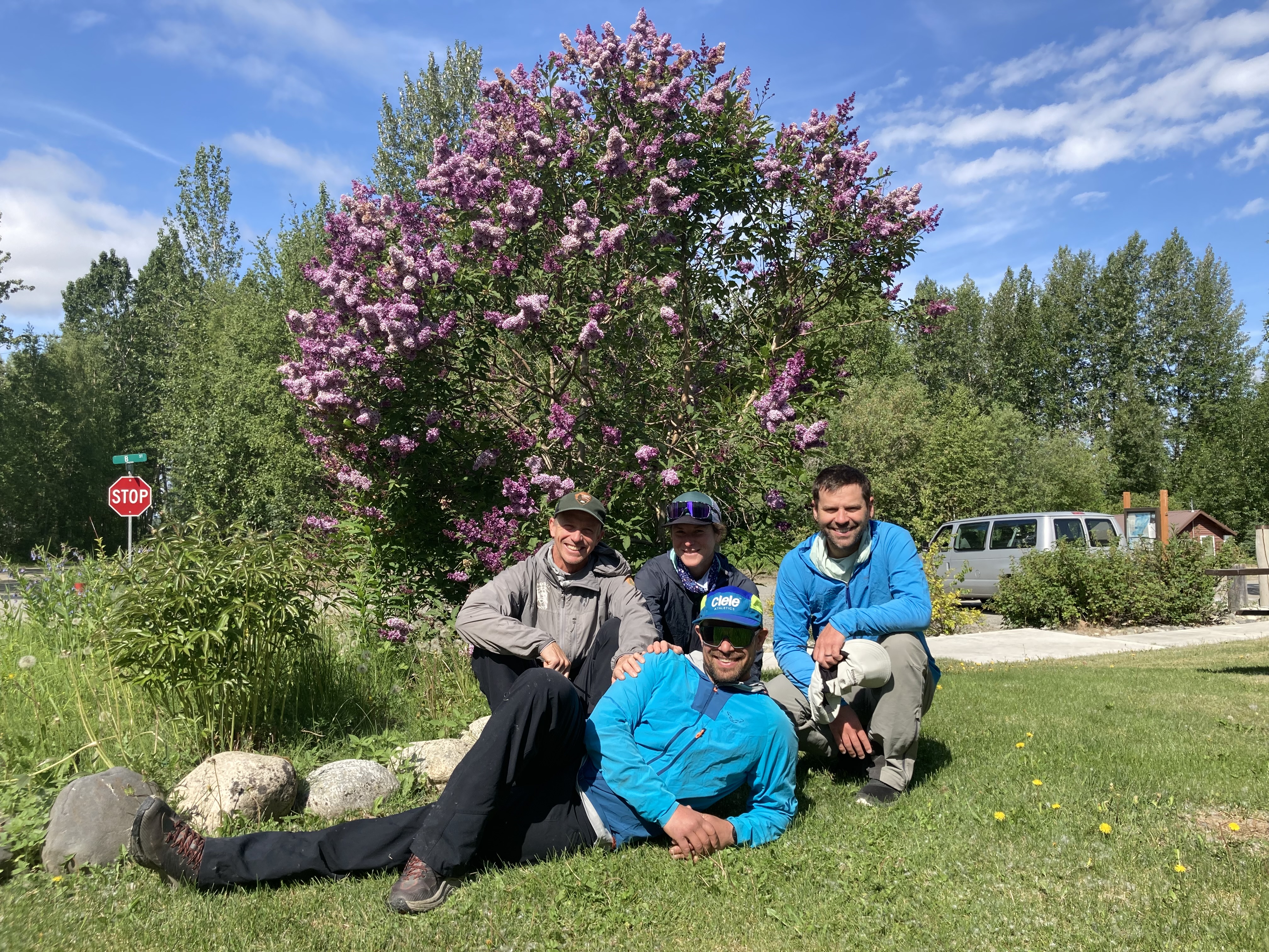 Final 14K patrol Four climbers sit on a lawn in front of a flowering lilac tree