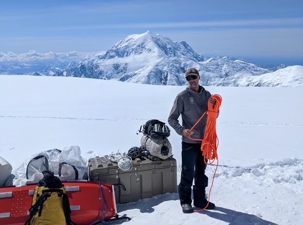 A man winds a spool of climbing rope with a snow peak in the background