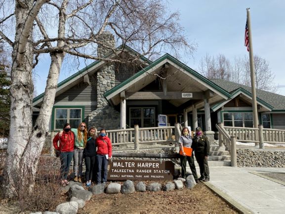 A team of mountaineers and two rangers stand outside the Talkeetna Ranger Station