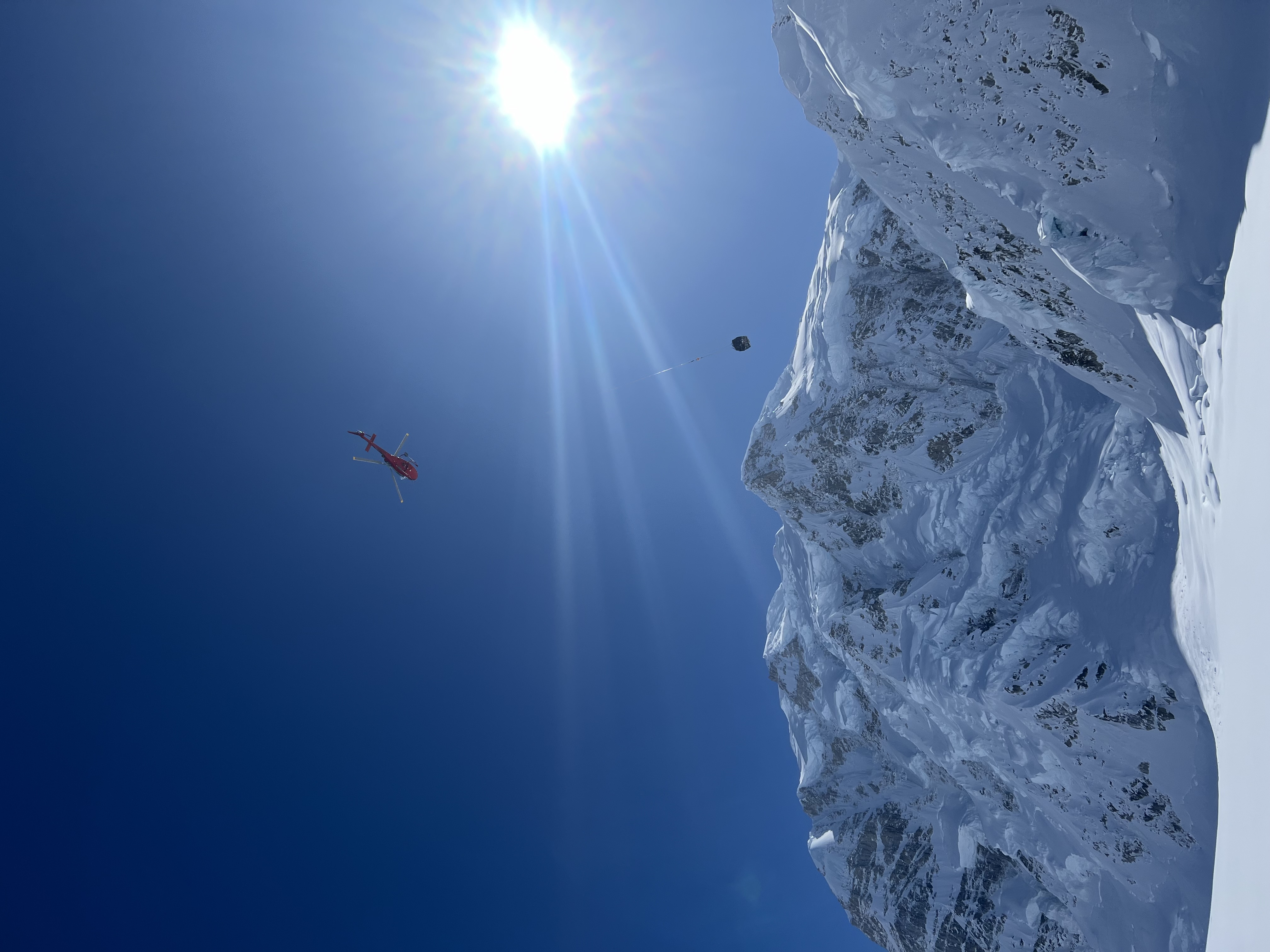 A helicopter flies past a snow-covered mountain hauling a cargo netload at the end of long rope line