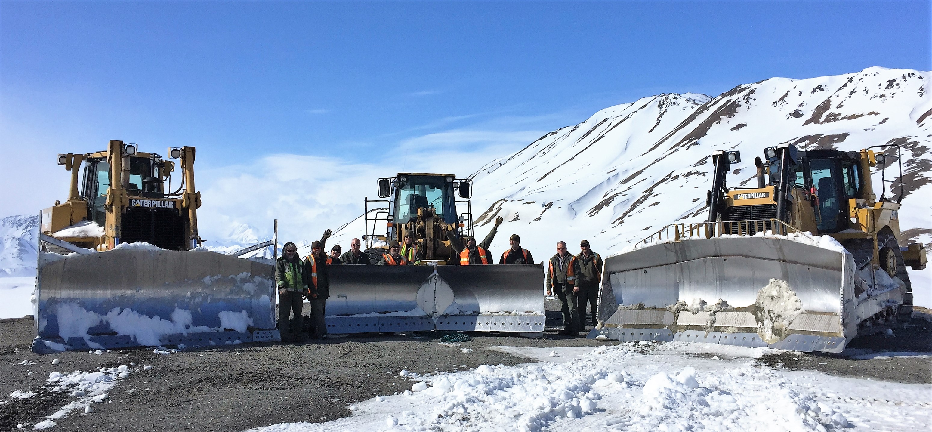 group photo of maintenance employees and large trucks on a dirt road