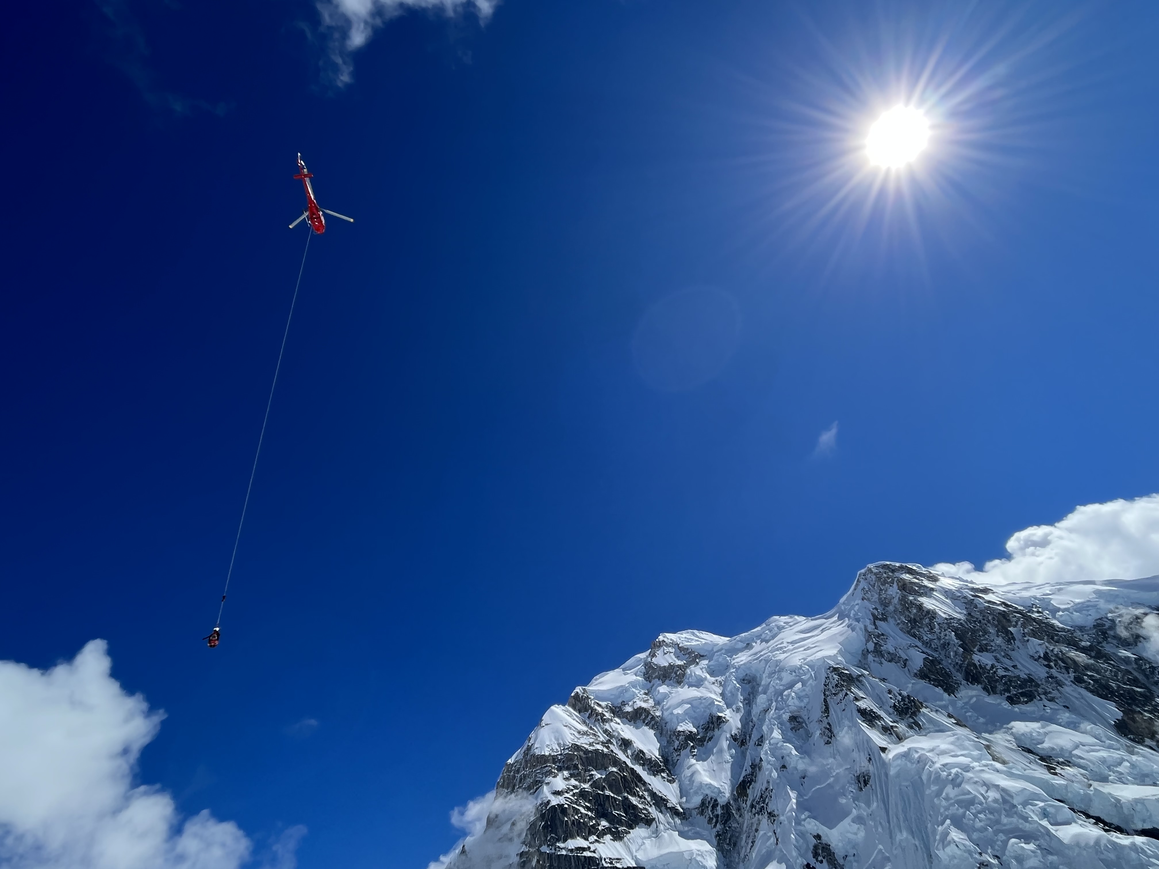Typical terrain short-haul training near Mount Hunter A helicopter flies with a ranger hanging at the bottom of a rope line