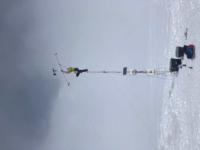 A climber scales a tall thin cross mounted with weather equipment