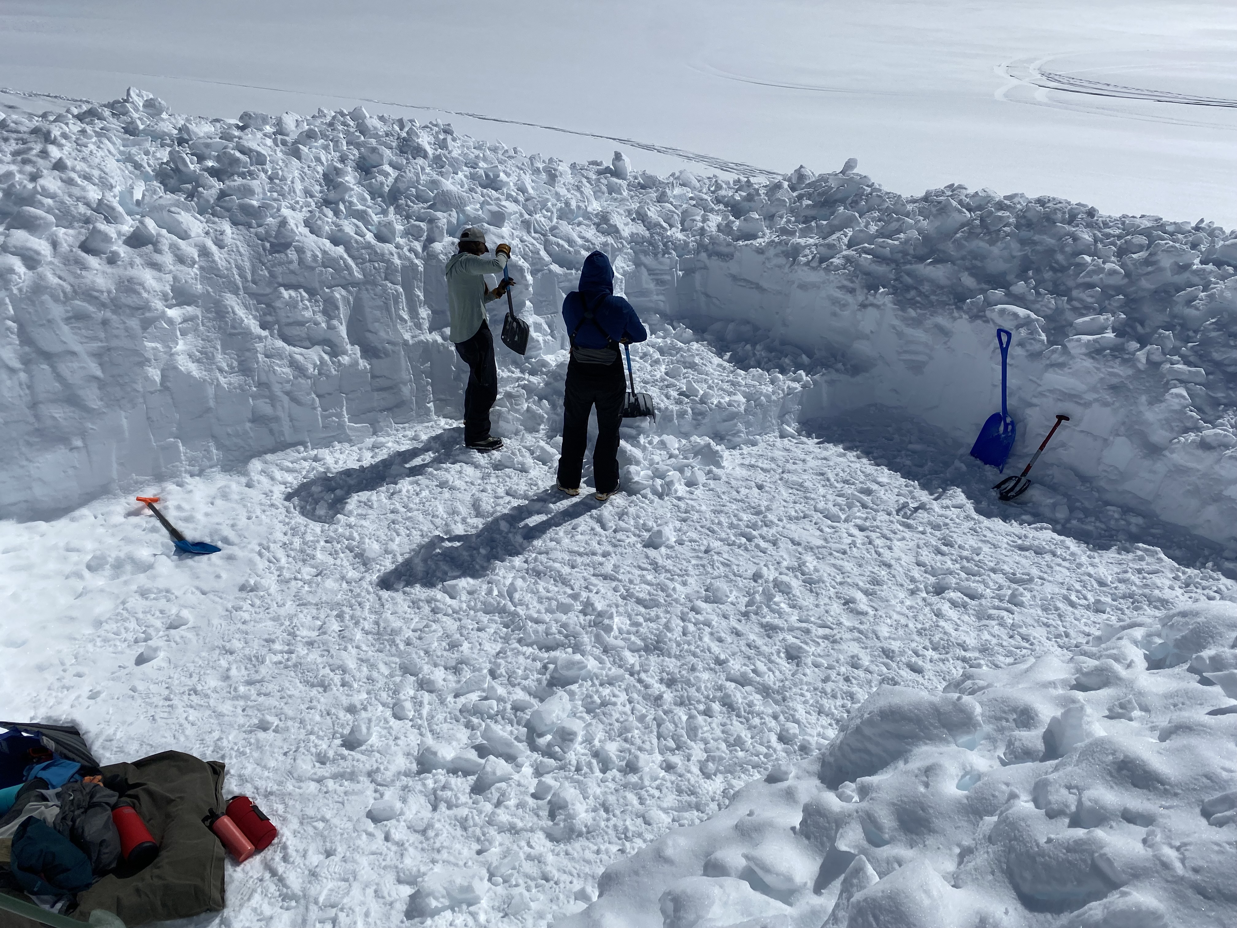 Two shovelers pause in the middle of large shovelled snow platform