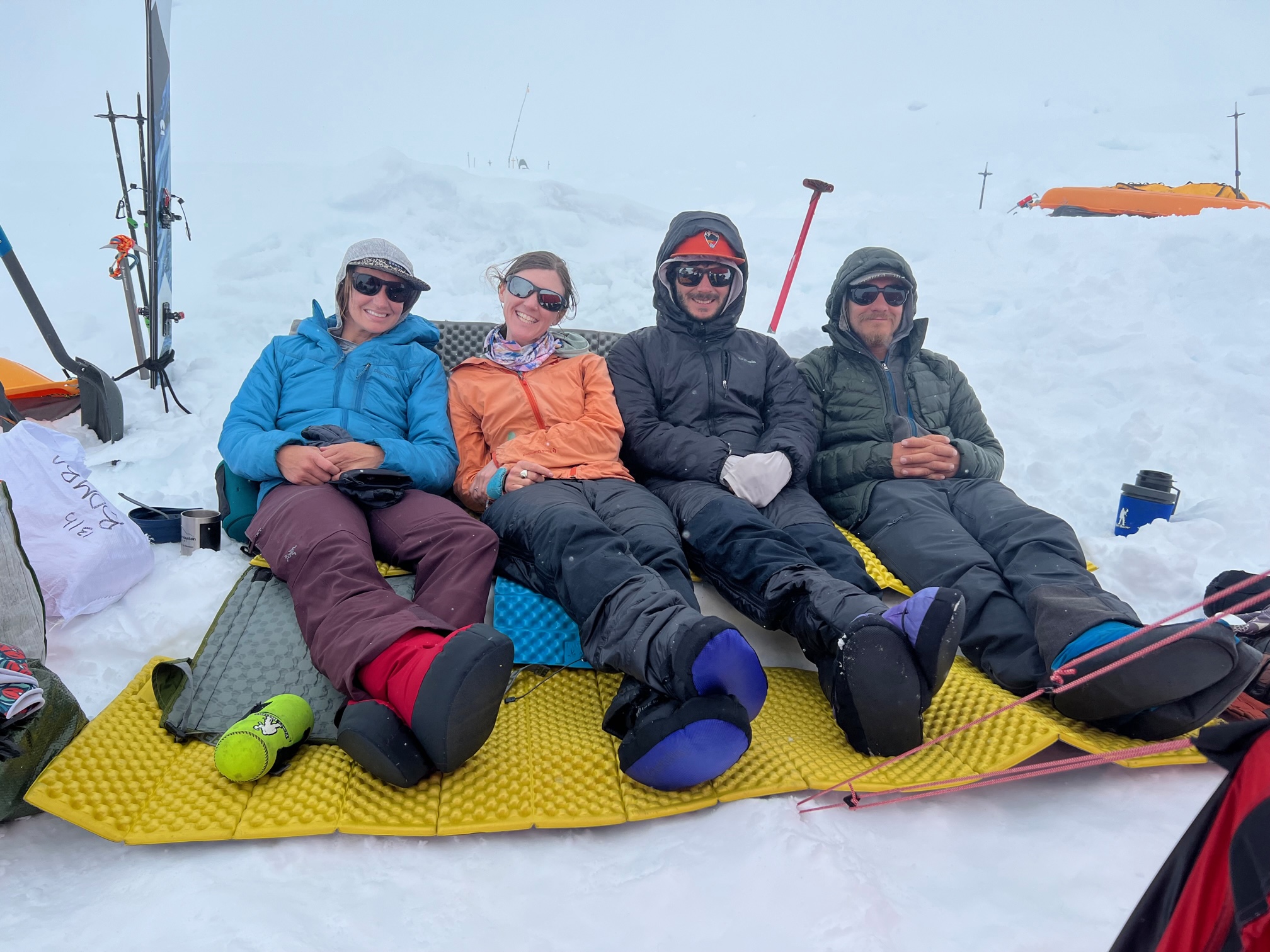 Four mountaineers relax on a makeshift sofa made of thermarest pads.