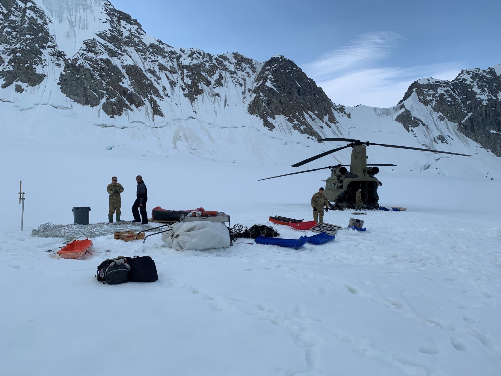 A Chinook heliicopter and members of its crew help load camp gear