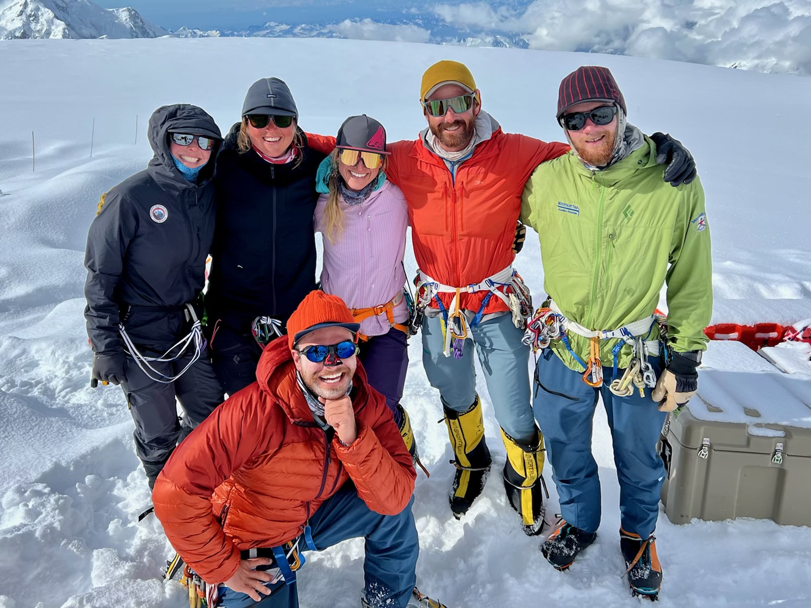 Six colorful mountaineers pose on a snowy glacier