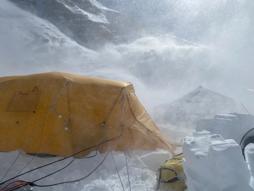 Windblown snow obscures a yellow tent