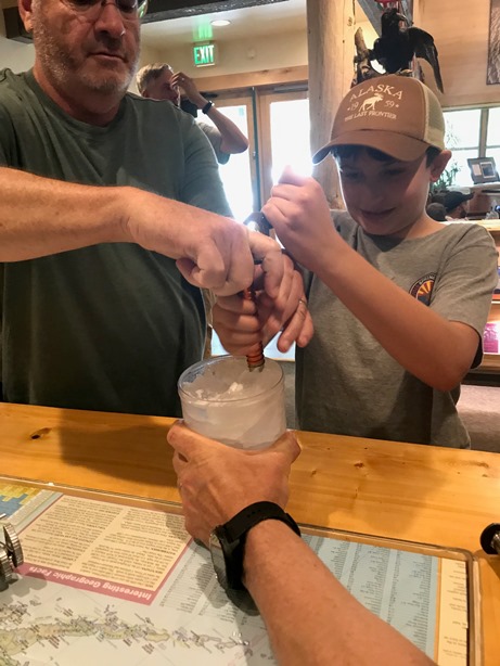 A boy and his father drill an ice screw into a block of ice