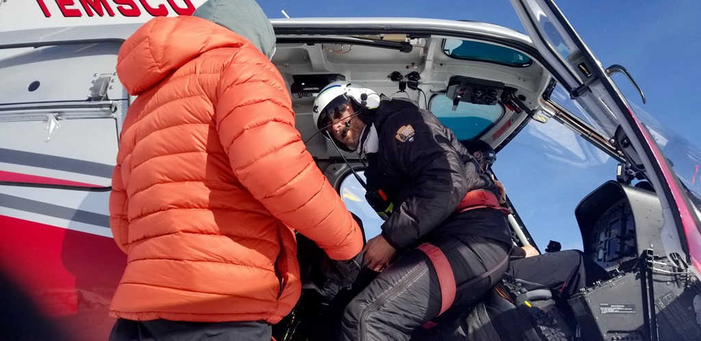 A park ranger assists a down-jacketed climber into a helicopter