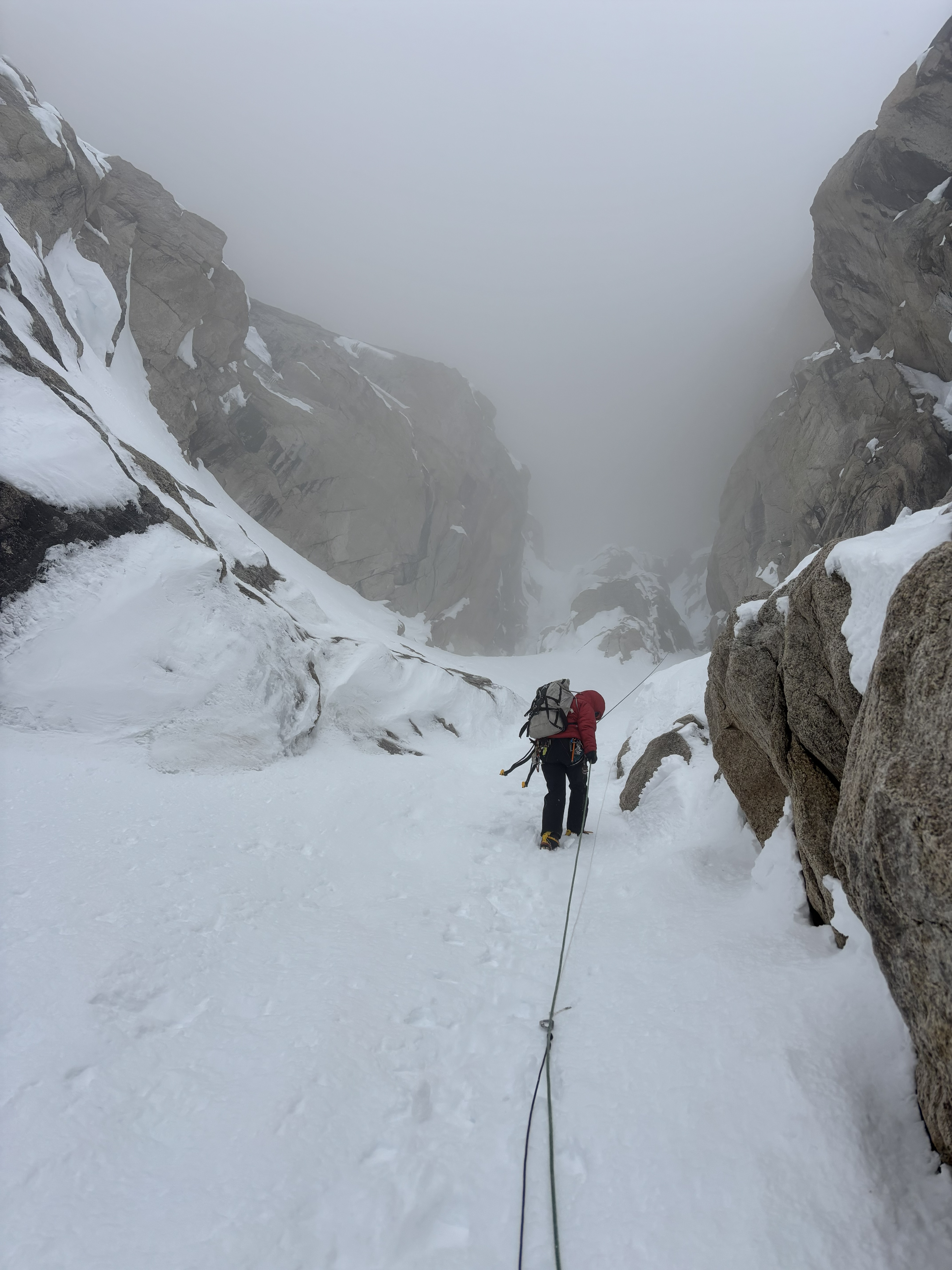 Looking back uphill, during the rappels A ranger in a road jacket climbs up a snow-covered pitch facing a foggy section