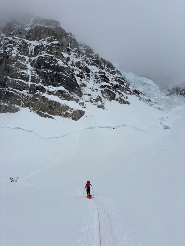 NPS Rangers approaching the base of the North Buttress A ranger makes their way across a snowy landscape toward a grey mountain.