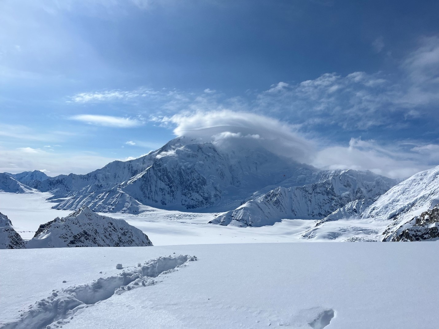 A sunny day at basecamp View of a snowy mountain against a bright blue sky with wispy clouds over the peak