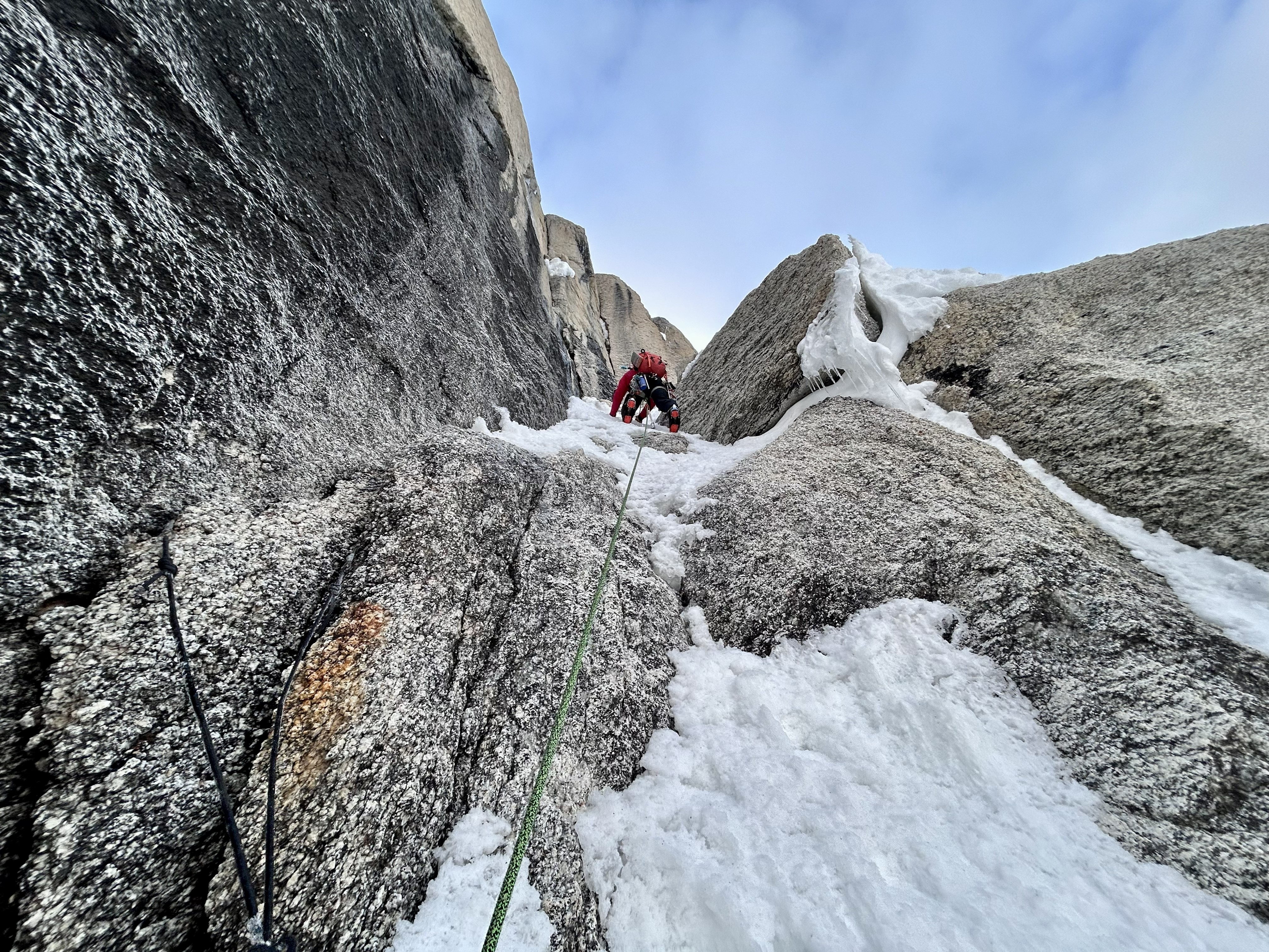 Mixed terrain Looking up at a ranger in a red coat climbing up a snowy rock pitch