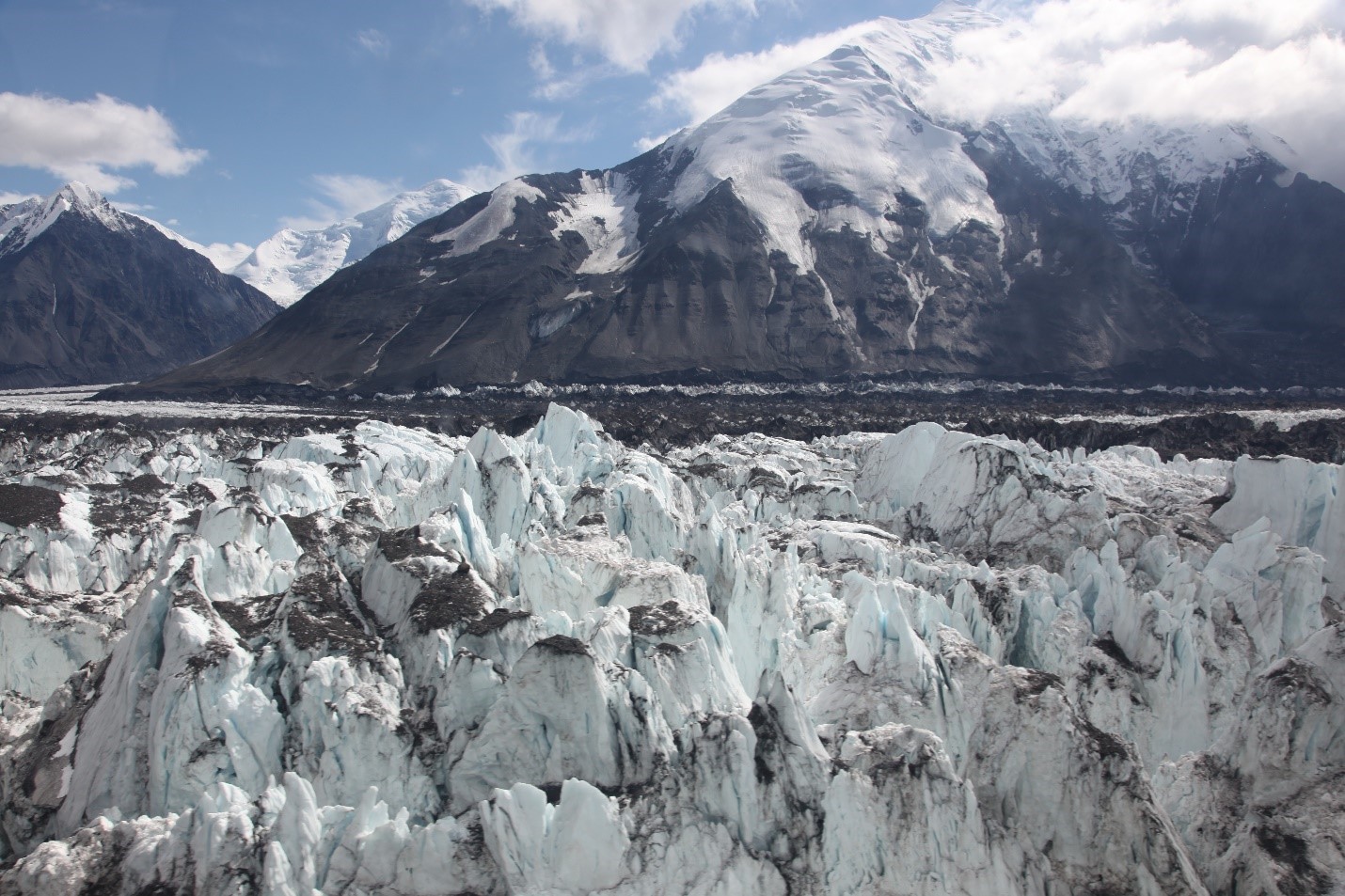 View of jumbled blue glacier ice in foreground with snow covered peak in distance