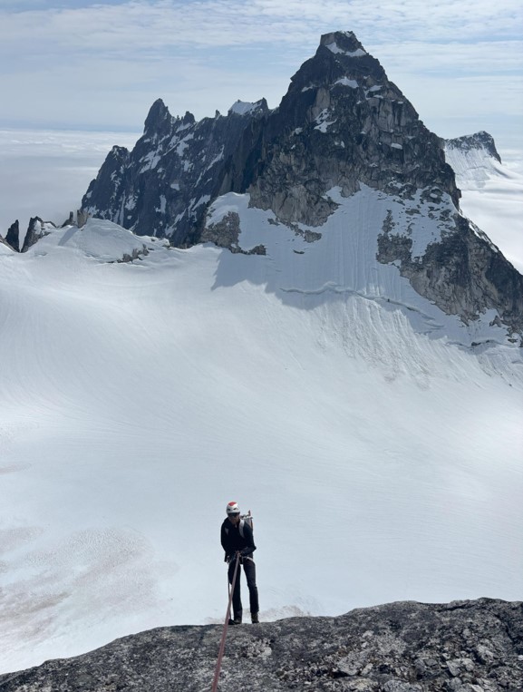 Nearing the last few rappels to the base of the route A ranger stands facing a mountain peak