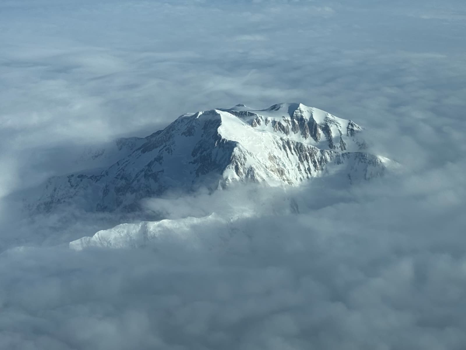 Two large snow-covered mountain peaks surround by clouds