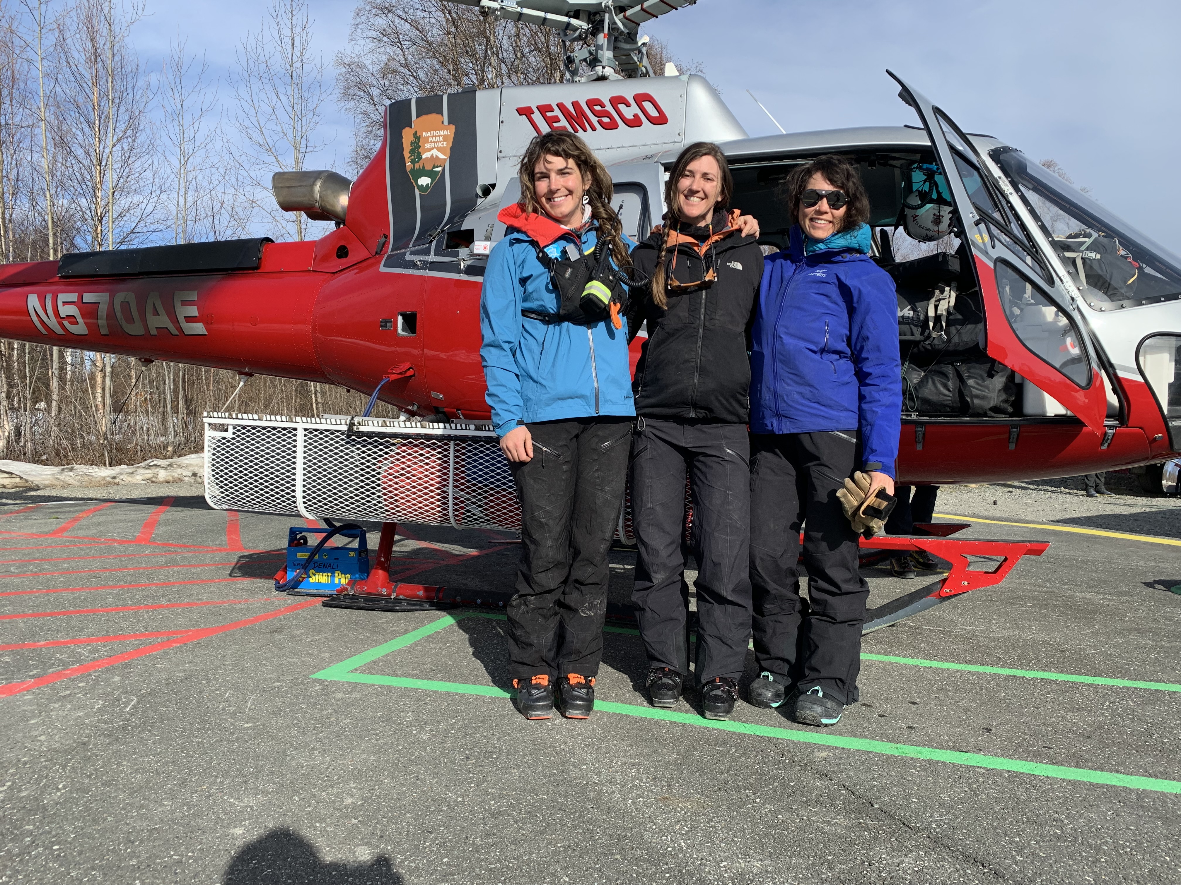 Three smiling climbers pose outside the NPS helicopter