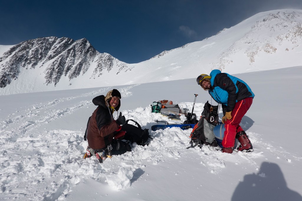 Two climbers about to set up camp on a bright snowy glacier