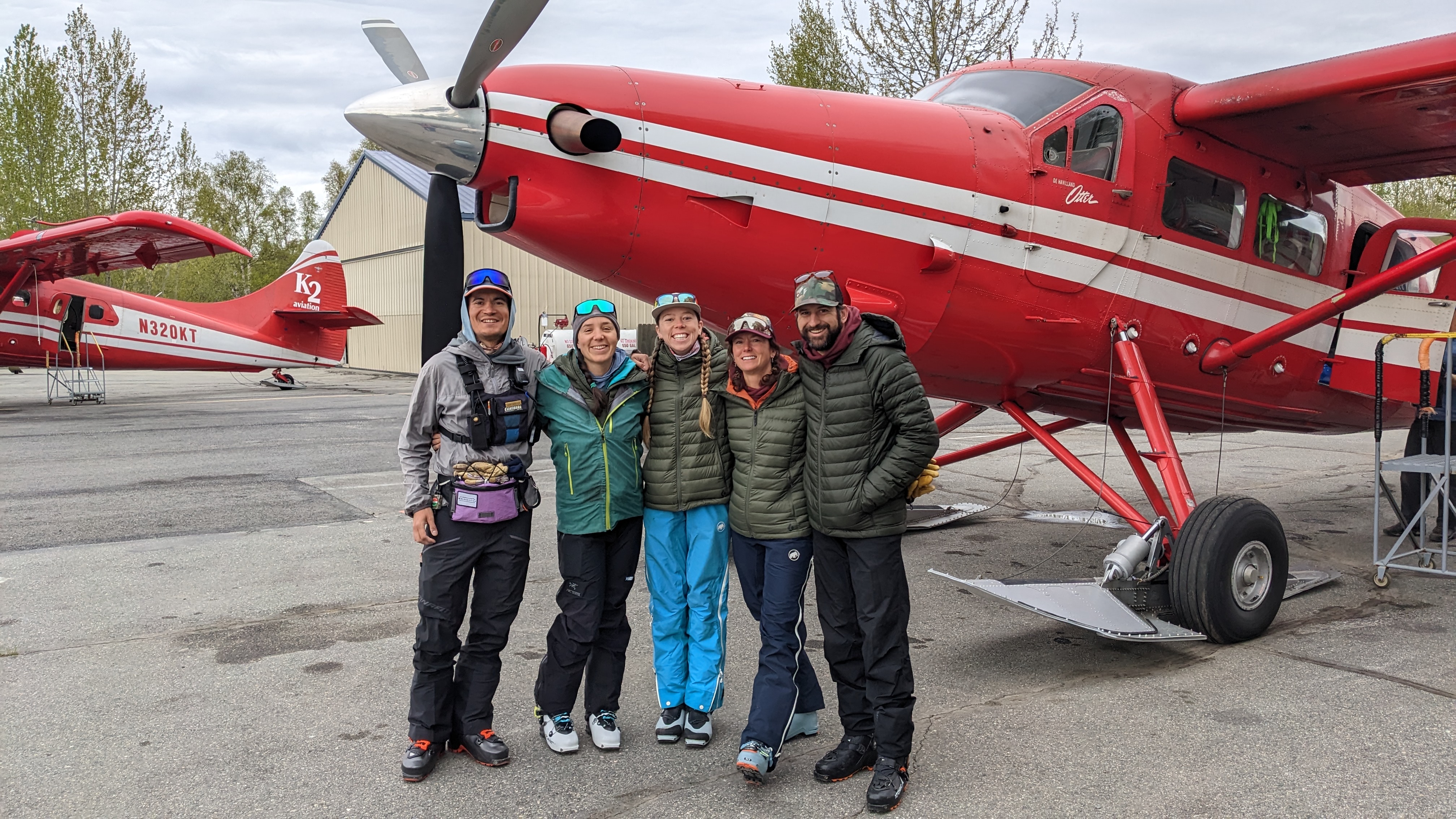 Five mountaineers pose outside a small airplane
