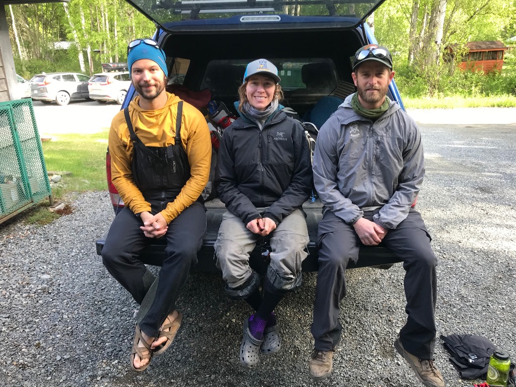 Three patrol members sit on the back of a pickup truck with gear