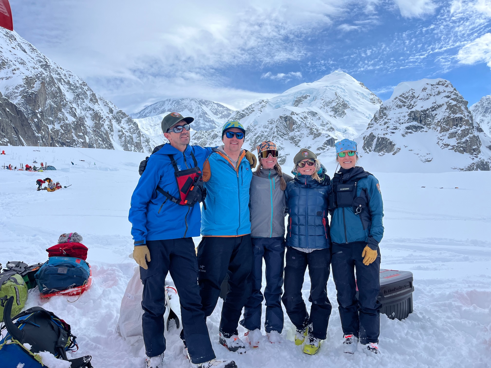 Five patrol members in blue stand on a glacier surrounded by mountain peaks