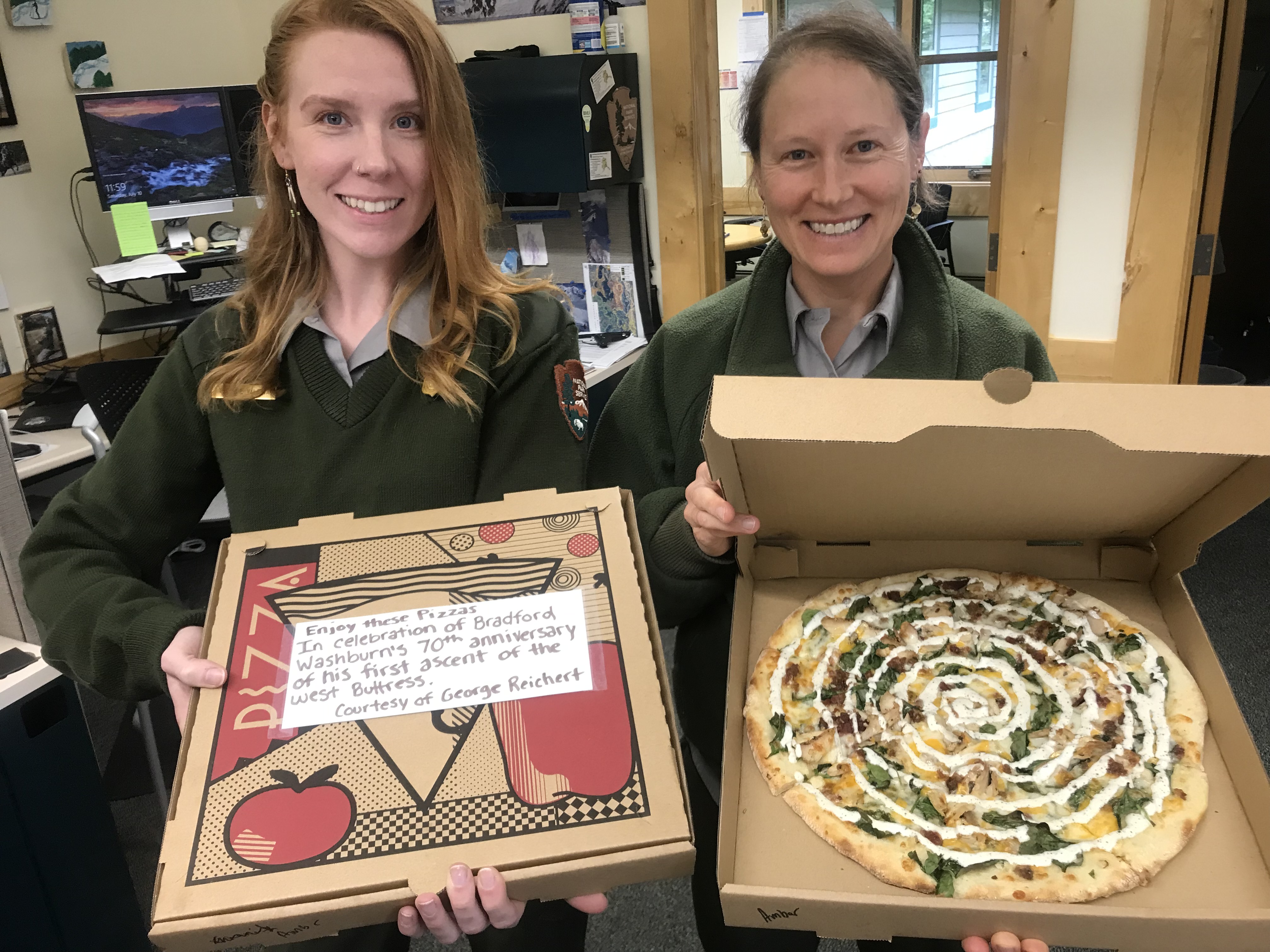 Two smiling rangers, each with a box of pizza