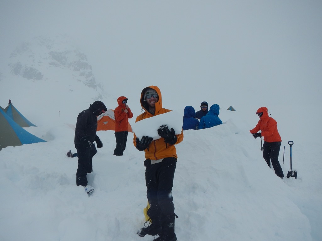 A team of seven climbers build an igloo under heavy cloud cover.