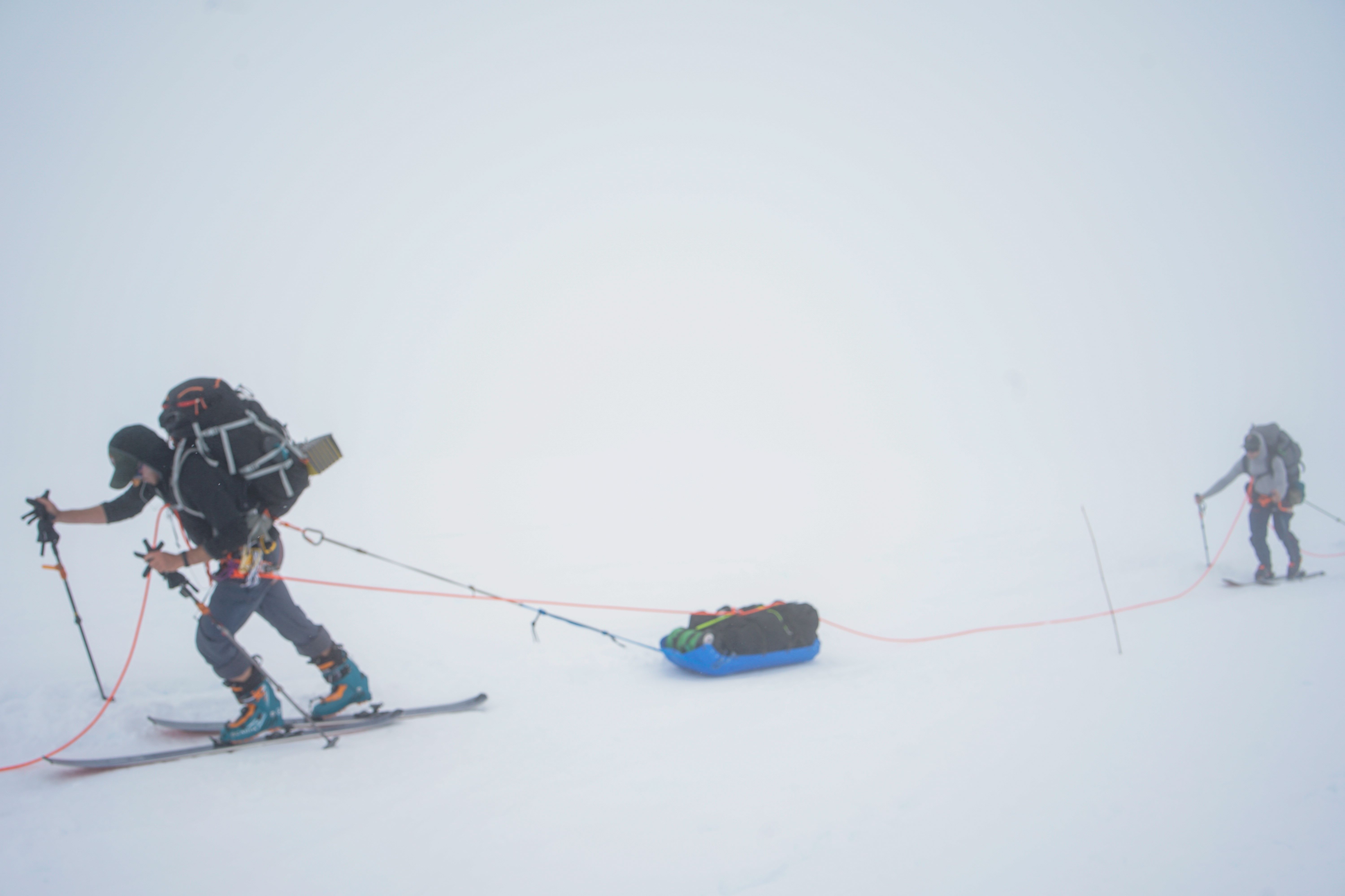 It's not all sweeping vistas Two roped climbers ski uphill in a whiteout, the lead climber pulling a heavy sled