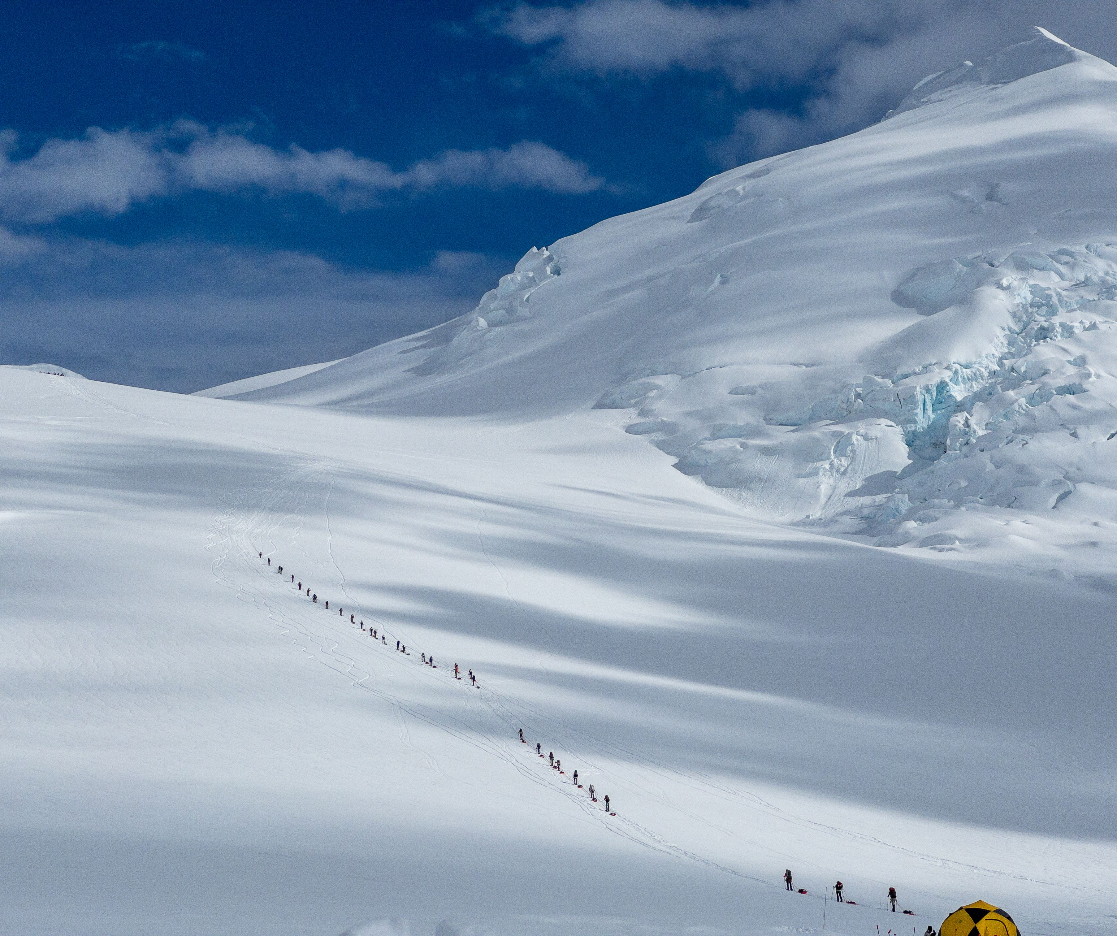 A long line of roped climbers ascends a glacier
