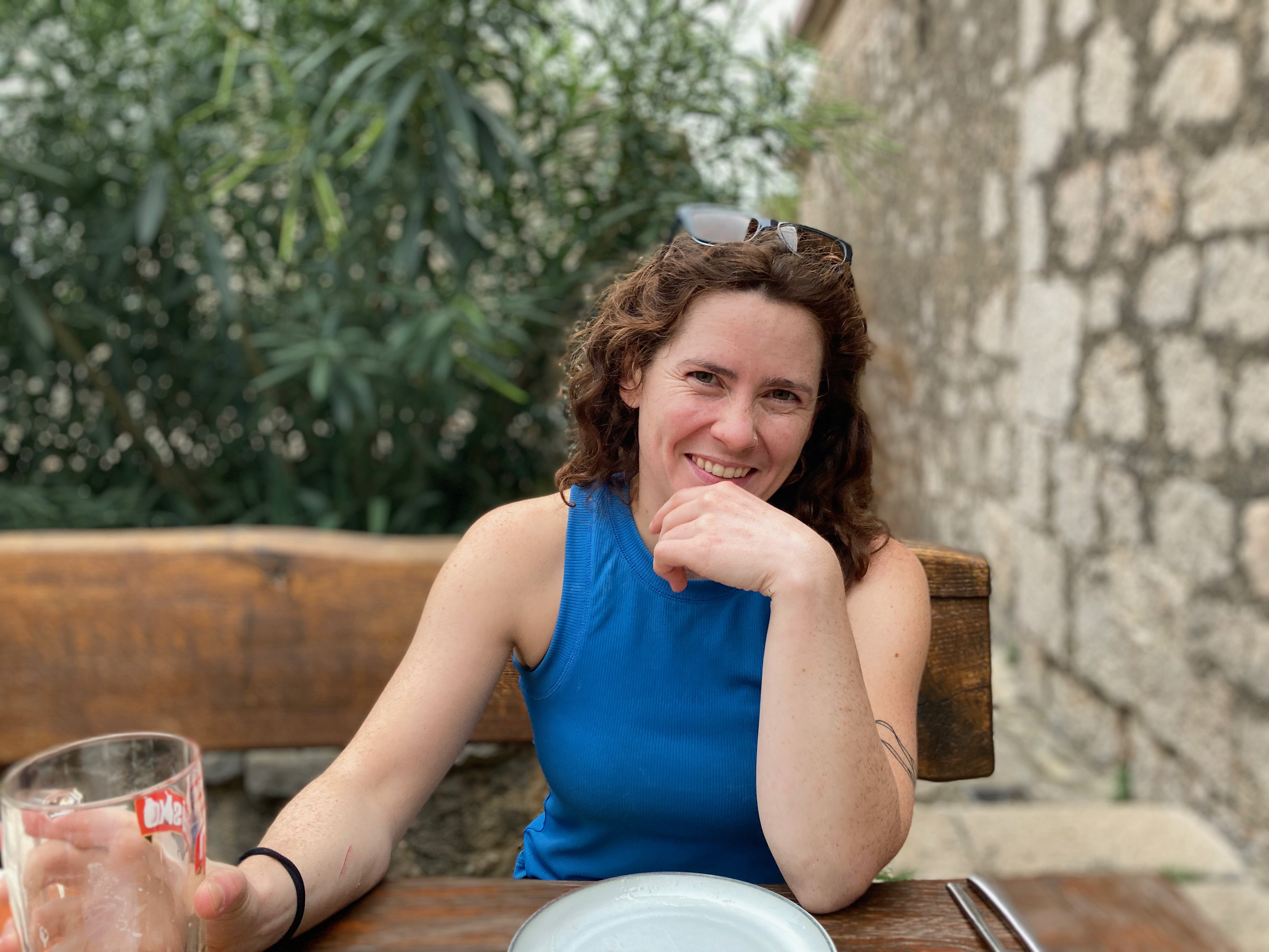 A woman with brown curly hair wearing a blue tank top sitting at a dinner table