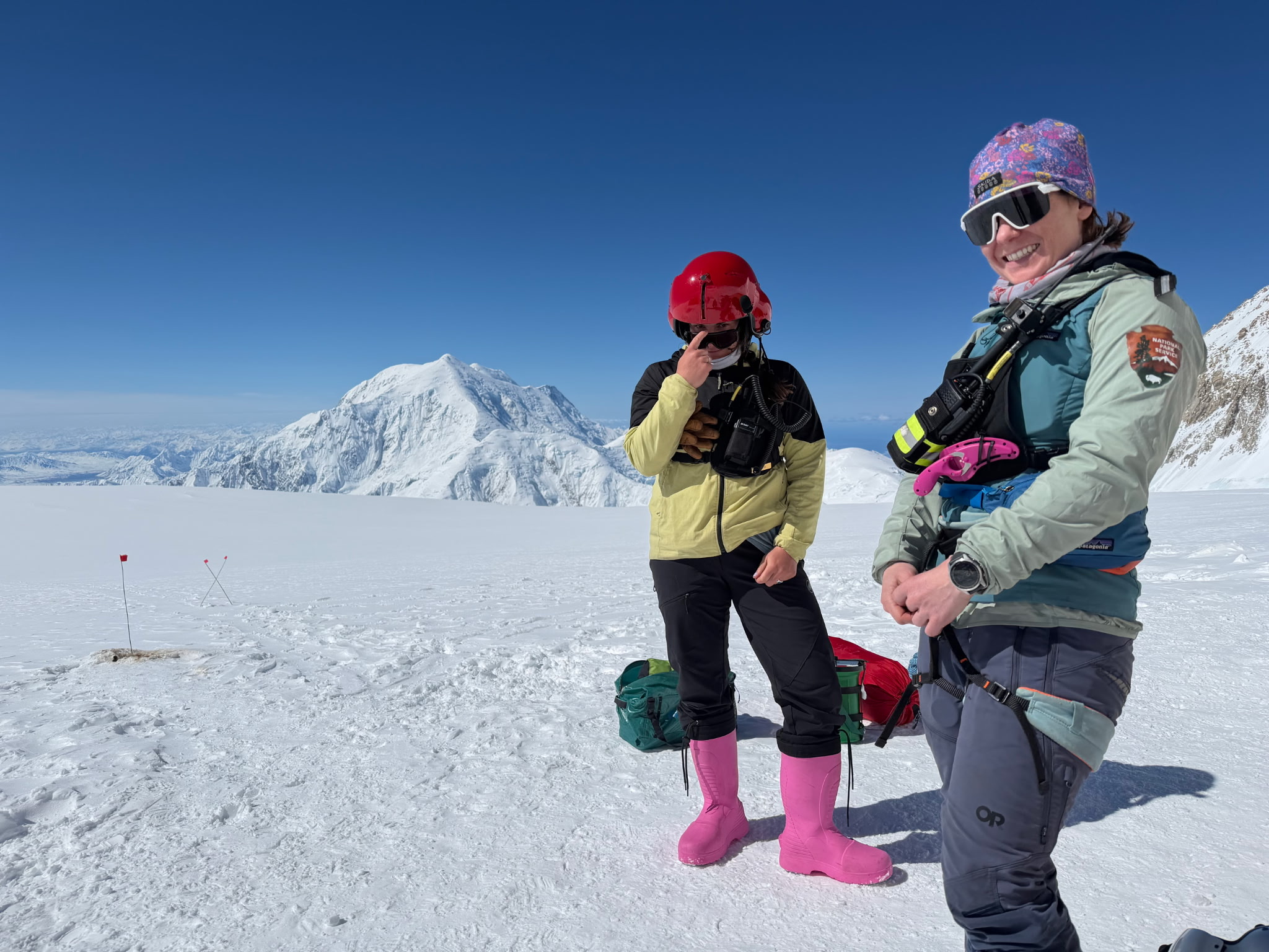 Two rangers in climbing gear, one of whom is wearing pink boots, on a snowy landscape