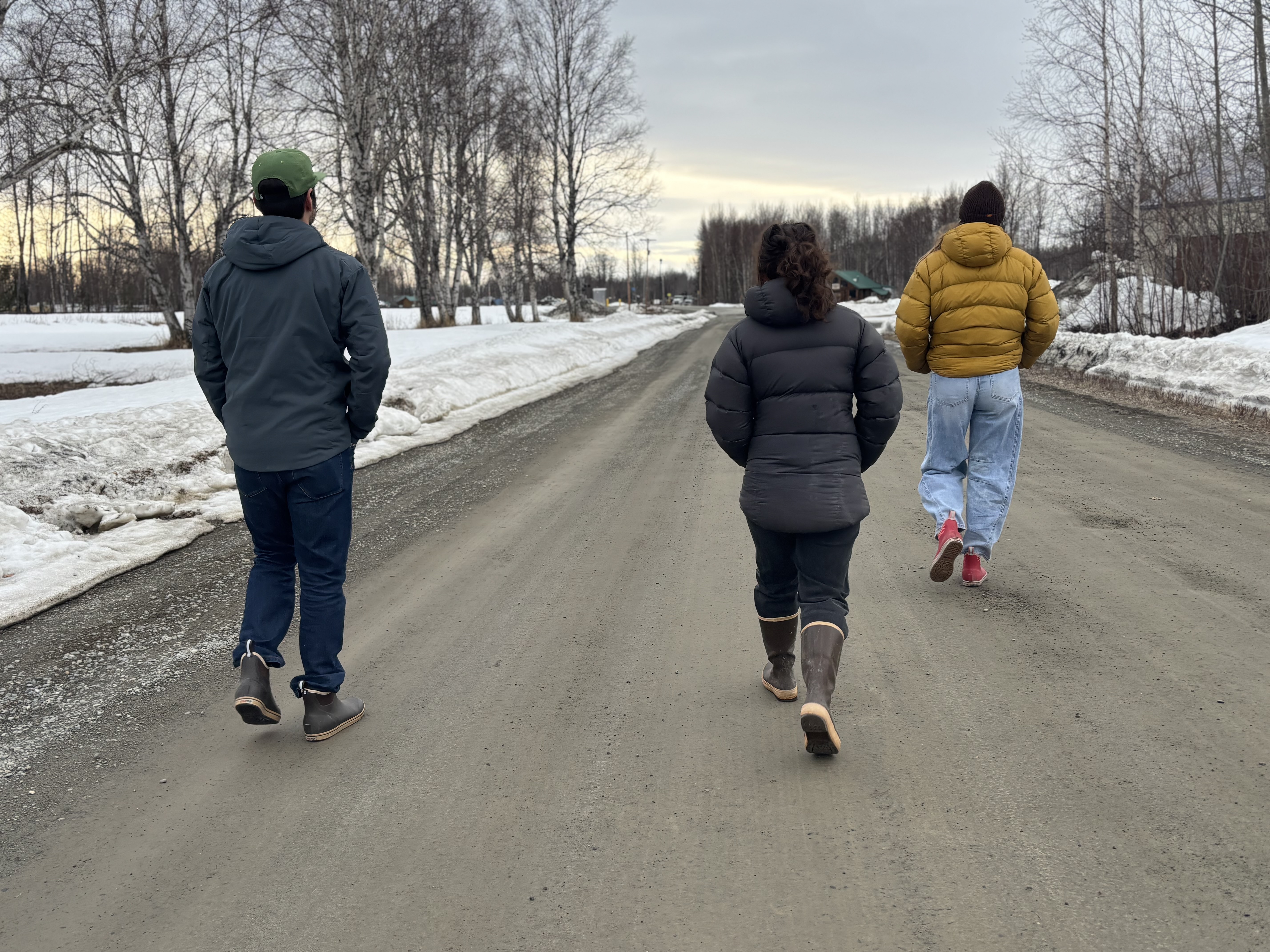 Three people walking away from the camera on a dirt road
