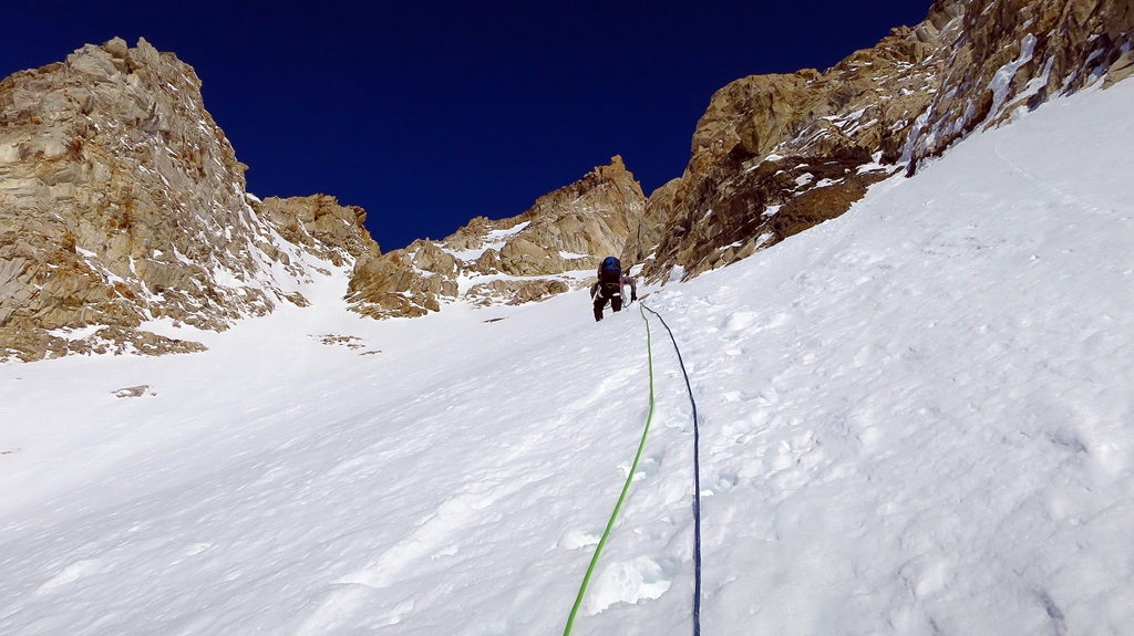 A roped climber ascends a steep snow field