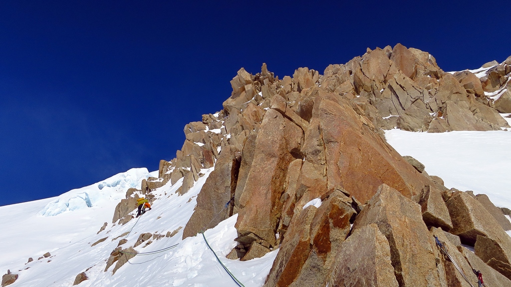 A roped climber reaches a rocky outcropping