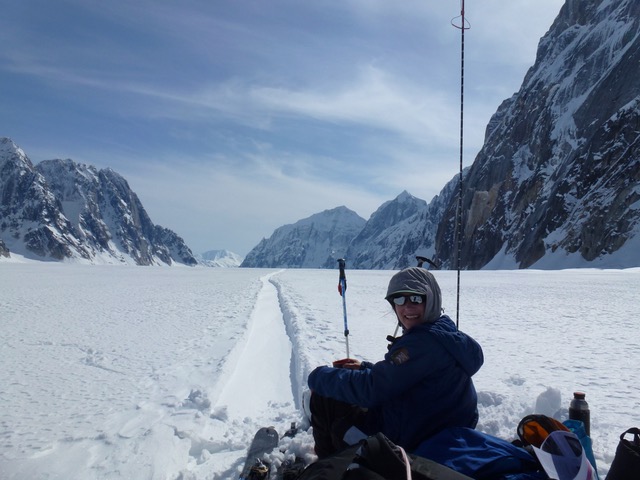 Ranger resting on her sled on a snowy glacier surrounded by granite peaks