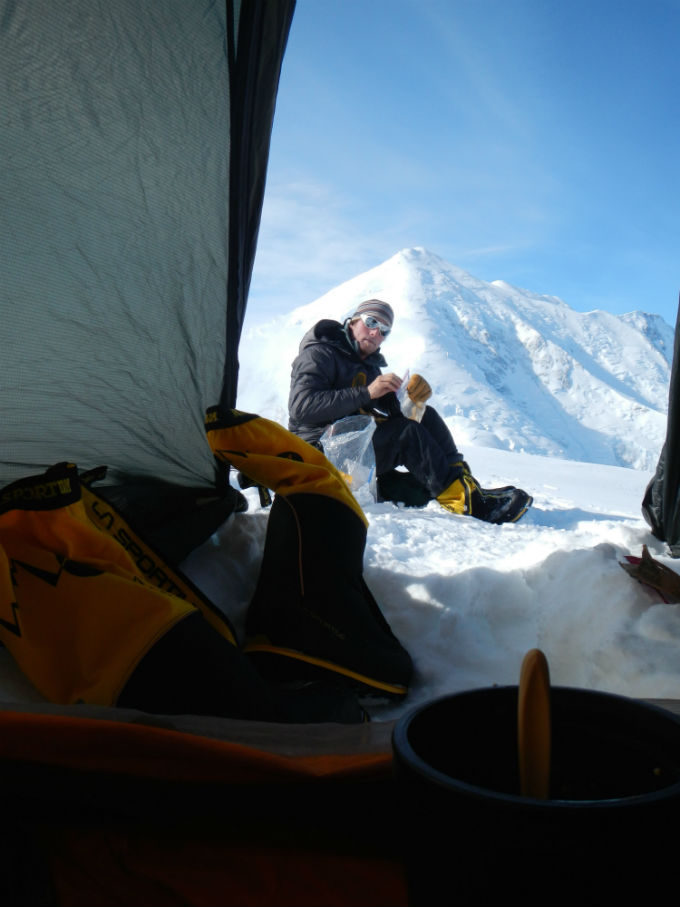 Looking out a tent to a snacking climber seated in the snow Looking out a tent to a snacking climber seated in the snow