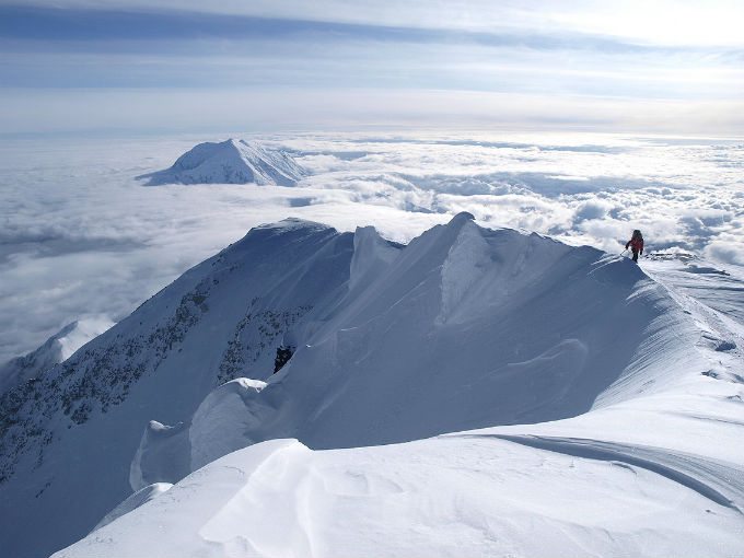 A climber approaches the summit Denali along a steep snowy ridge