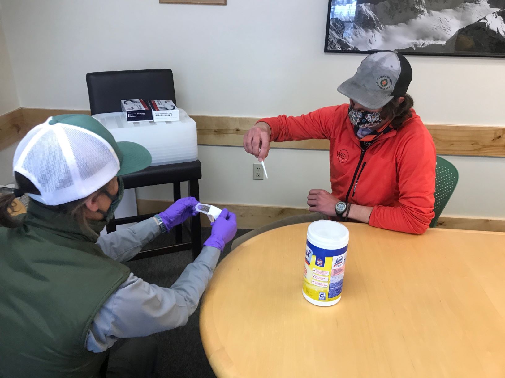 Preparing for the COVID swab Two seated, masked climbers open a swab kit