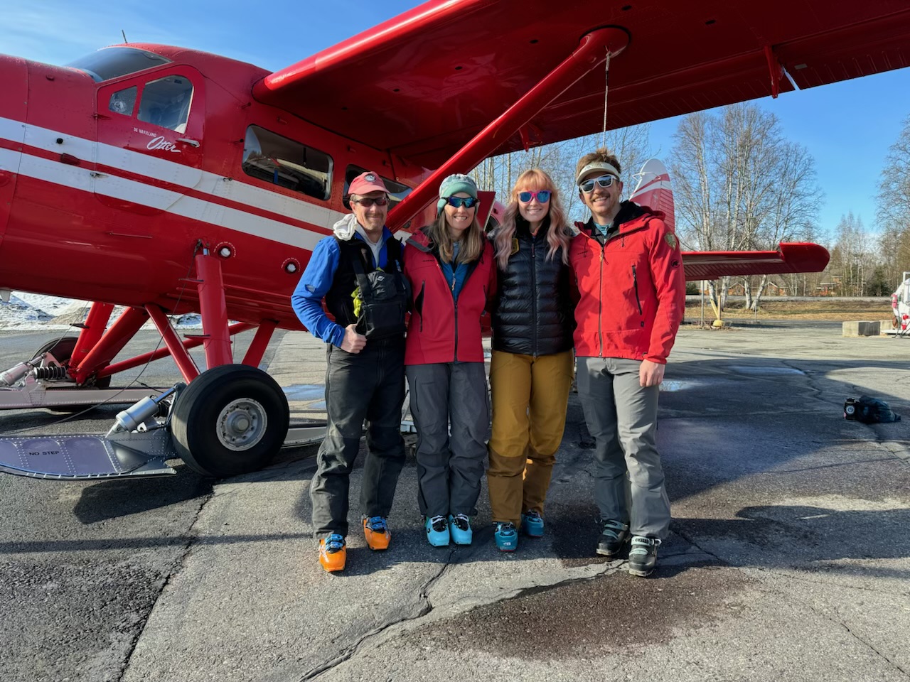 Four mountaineeris stand outside a red airplane