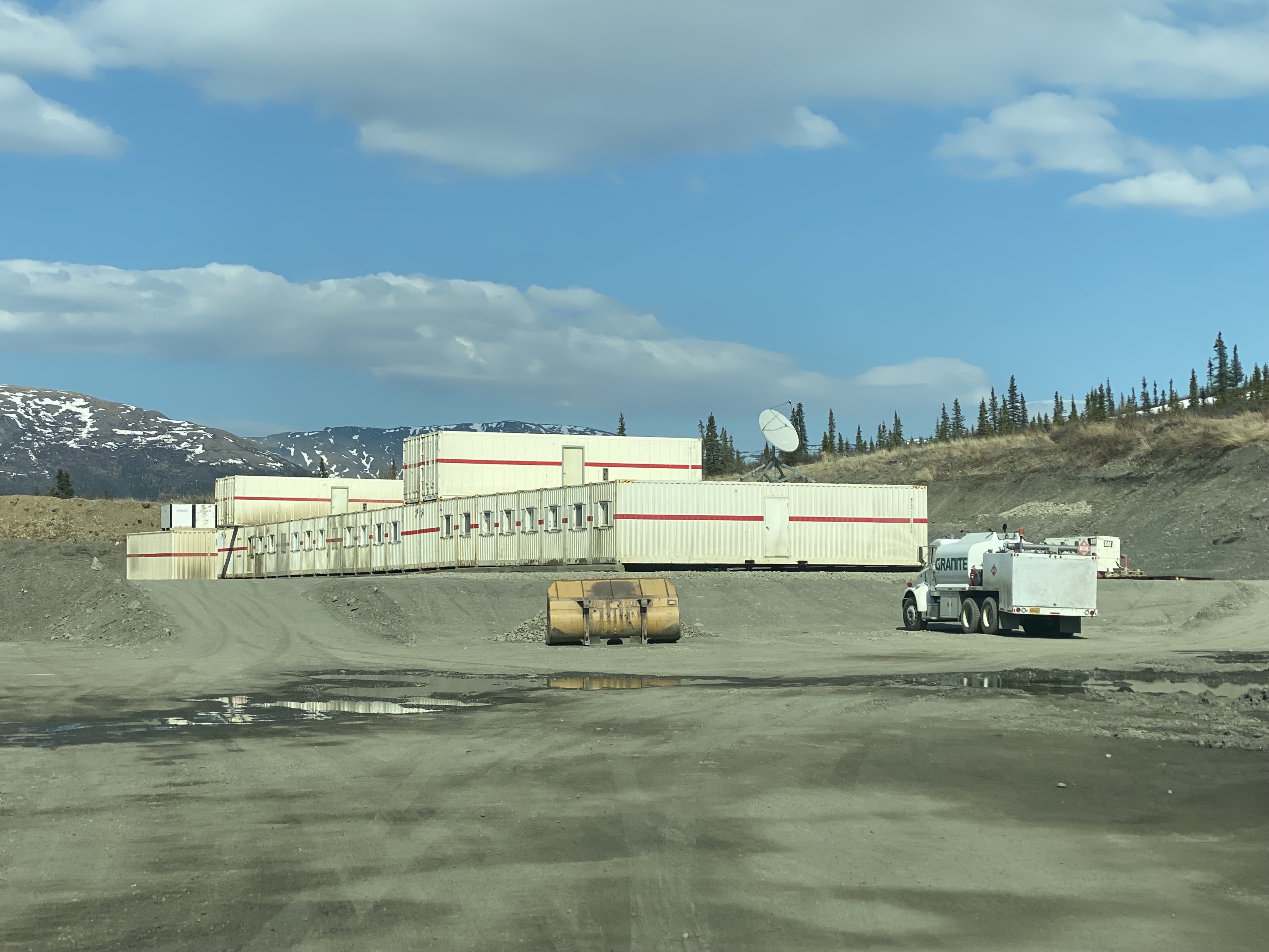 Tek Pit housing camp Many mobile trailer buildings are connected side by side into a large unit. The unit is located in a large gravel pit with a few construction vehicles parked nearby.