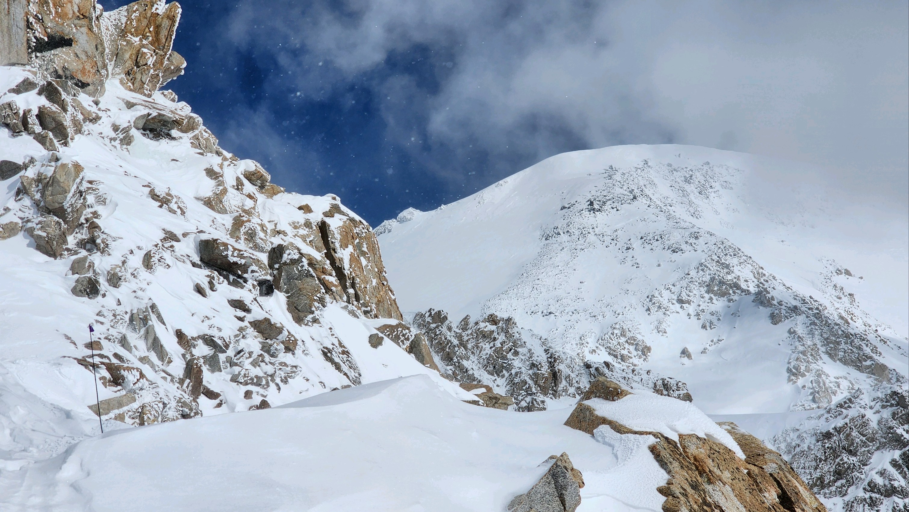 View of snow and rock ridge with a single flagged wand visible