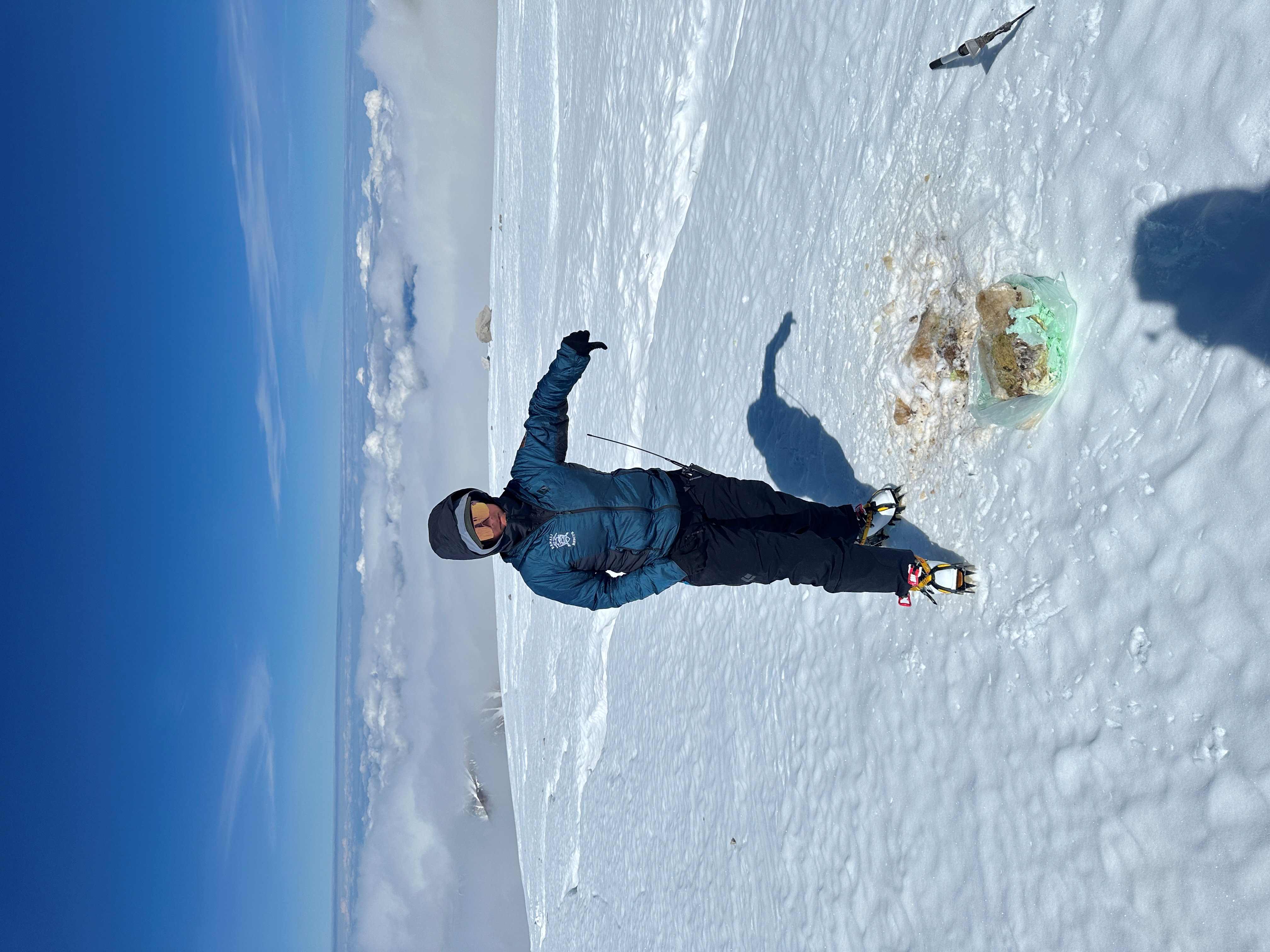 Big thumbs down A ranger in a puffy jacket stands on a glacier displaying a big 'thumbs down' over a dirty pile on the glacier