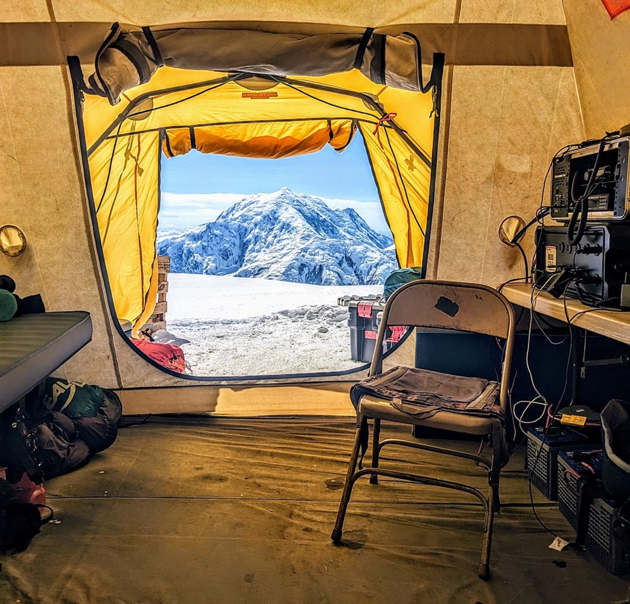 The Ranger Chair View looking out a yellow tent at a mountain in the distance. A metal folding chair and a radio console sits inside the tent.