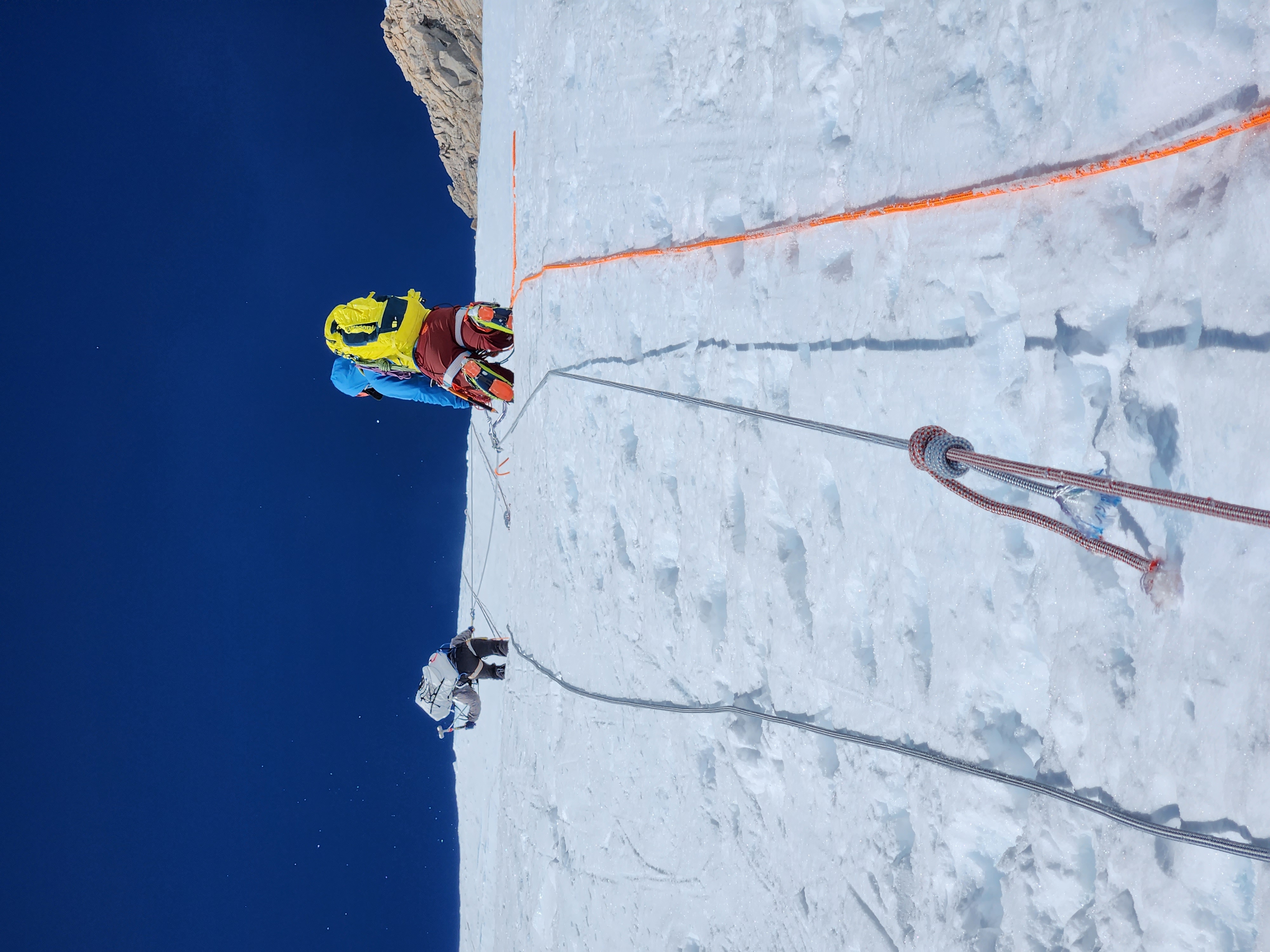 A view from below of two climbers ascending a roped slope.